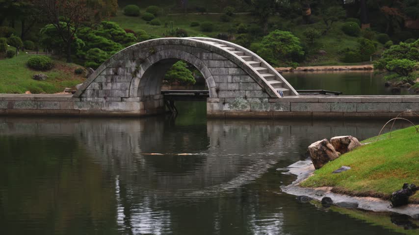 Shukkeien traditional Japanese garden in Naka-ku,  Shukkei-en garden, Hiroshima city, Chugoku region, Japan, with pond and trees, thatched roof teahouse pavilion reflection in a rainy autumn day