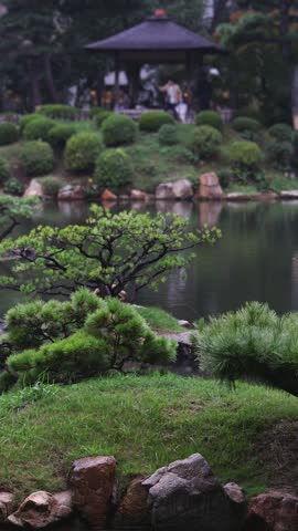 Shukkeien traditional Japanese garden in Naka-ku,  Shukkei-en garden, Hiroshima city, Chugoku region, Japan, with pond and trees, thatched roof teahouse pavilion reflection in a rainy autumn day