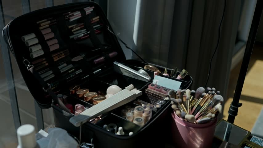 Makeup artist kit open with palettes lipsticks and a pot of brushes beside a ring light