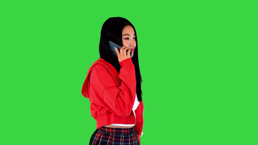 Carefree asian woman walks talking on the mobile phone on a Green Screen, Chroma Key.