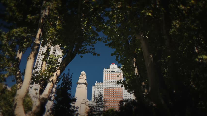 Leafy view of Madrid landmark buildings rising above the trees near the Cervantes Monument in Plaza de Espana.
