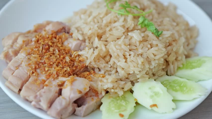 Close-up of tender chicken and fragrant rice topped with crispy garlic and drizzled with savory dipping sauce, presented as a classic Asian-style meal.