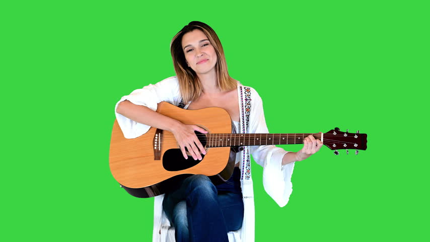 Smiling lady plays acoustic guitar and sings a song on a Green Screen, Chroma Key.