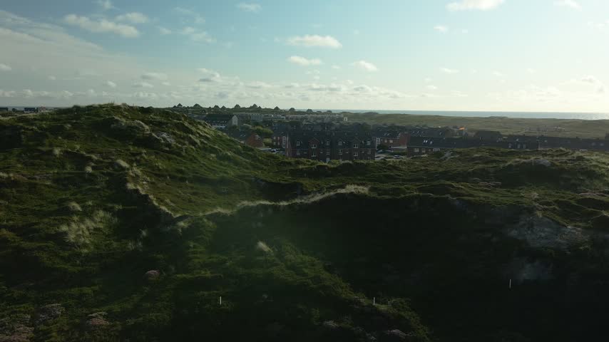 Low drone flight across a dune ridge at Hornum on Sylt with marram grass in the foreground and the apartment houses of the village behind