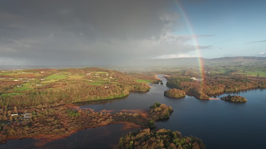 Aerial view of a lake with small islands and autumn foliage under a rainbow and stormy sky in Sligo, Co. Sligo, Ireland.