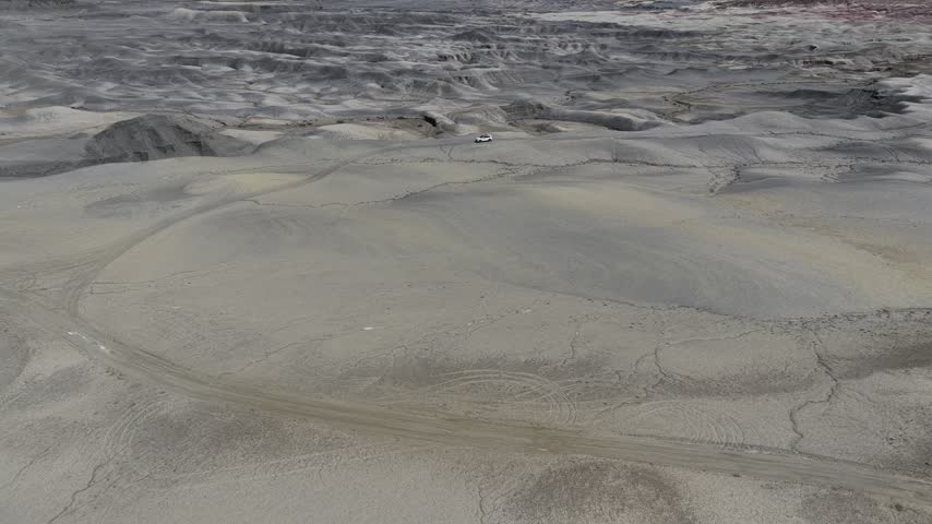 Aerial view of Moonscape Overlook featuring grey desert terrain and a vehicle on a dirt road in Hanksville, Utah, United States.