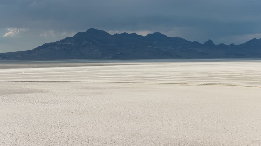 Aerial view of the vast white salt crust of the Bonneville Salt Flats under a dramatic stormy sky in Tooele County, Utah, United States.
