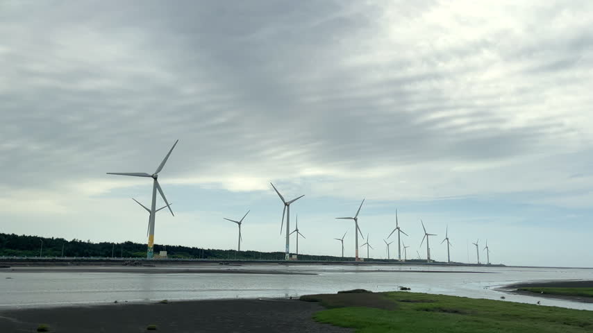 Rows of wind turbines line the shoreline behind wetland water channels at Gaomei Wetlands in Taichung, Taiwan.