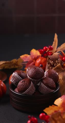 Delicious homemade chocolate muffins in a ceramic bowl, arranged for a halloween party with festive autumn decorations, pumpkins, fall leaves, and a spooky glowing jack o