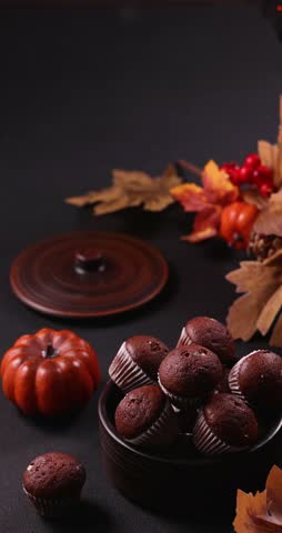 Delicious homemade chocolate muffins served in a ceramic bowl on a dark table, decorated with autumn leaves, pumpkins, and a glowing lantern for a cozy halloween or thanksgiving celebration