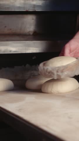 Bread dough is placed on a wooden baking board before being transferred to the oven. The dough pieces are arranged on the board for baking.