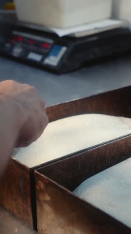 Bread dough is scored with a small blade while resting in a metal baking tray. Several prepared dough pieces can be seen in the surrounding trays during the baking preparation process.