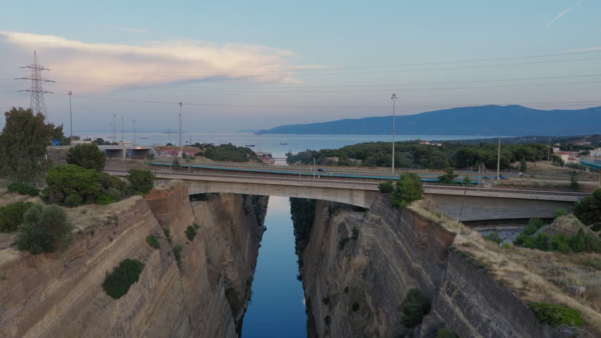 Low drone pullback over Corinth Canal and highway bridge at sunset, Greece, aerial