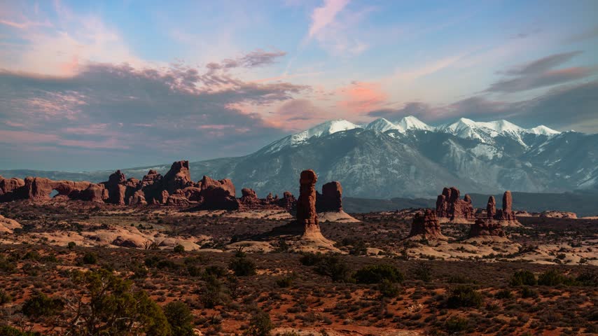 Sunset time lapse of colorful clouds over Arches National Park with snow capped La Sal and Rocky Mountains. Utah, USA