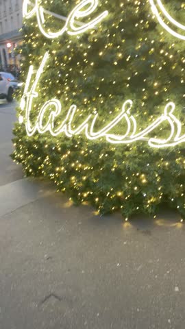 giant Christmas tree in Paris illuminated with neon lettering lights in front of a blue evening sky creating a festive holiday atmosphere, 4k vertical