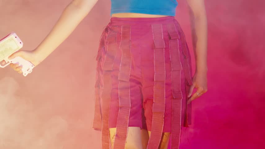 Detail shot of a pink money gun held by a woman amidst thick, atmospheric smoke.