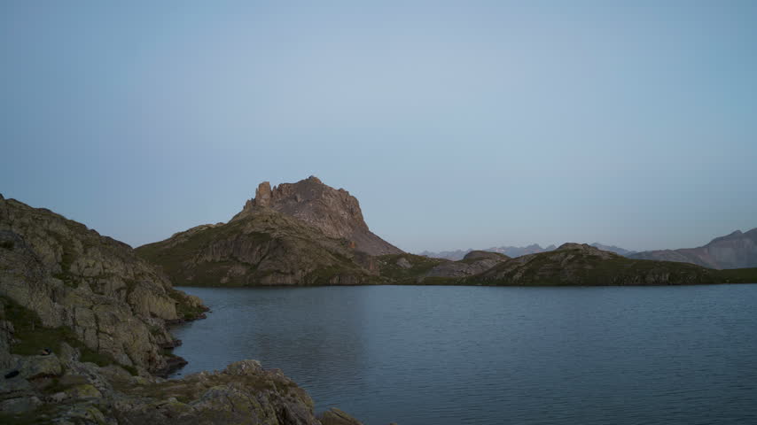 Twilight deepens over Lago Superiore di Roburent as stars and the Milky Way appear above the still alpine lake in timelapse.