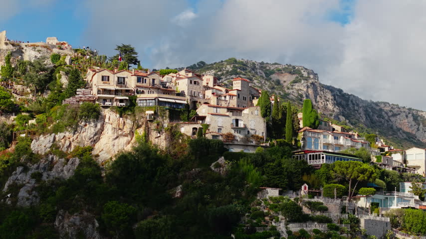 Hilltop stone village overlooking cliffs and lush greenery on a partly cloudy day