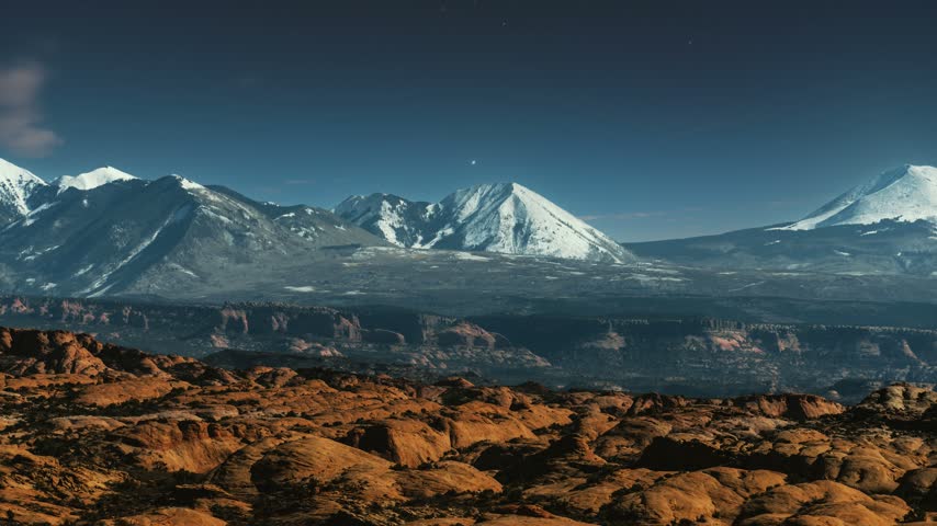 Night time lapse of Arches National Park desert landscape with La Sal Mountains under a starry sky.