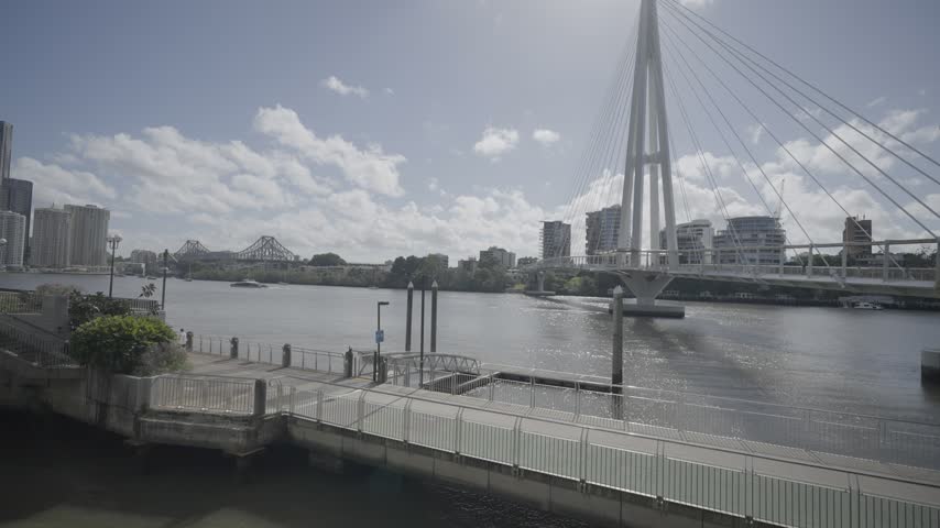 A riverside boardwalk leads toward the Kangaroo Point Bridge with the Brisbane city skyline beyond.