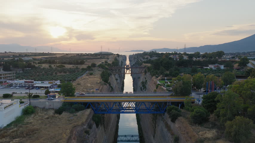 Sunset flight above Corinth Canal stretching across the Isthmus of Corinth, aerial static medium as cars and buses drive