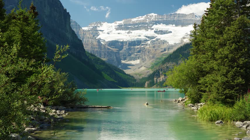 Lake Louise summer landscape with tourists canoeing on turquoise water under Victoria Glacier. Banff, Alberta, Canada.