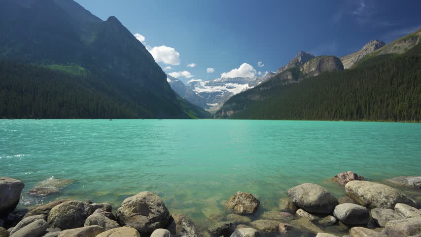 Lake Louise summer landscape with tourists canoeing on turquoise water under Victoria Glacier. Banff, Alberta, Canada.
