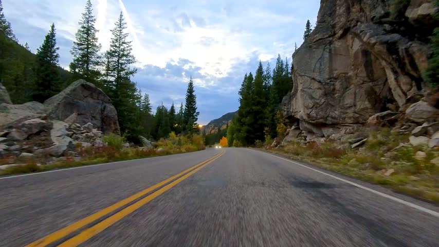 POV driving along a winding mountain highway surrounded by colorful autumn foliage at dusk in Colorado.