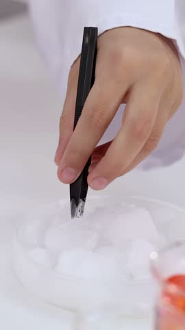 Close-up of a student using black tweezers to pick up white solids during science class.