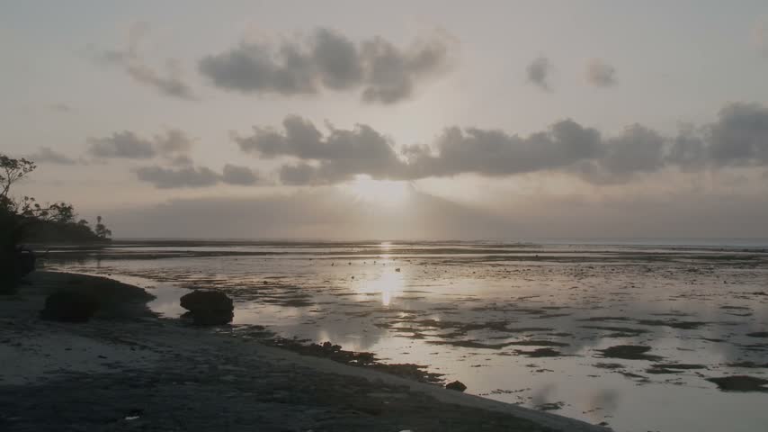 Beautiful tropical sunset over the exposed reef at low tide in G-Land, Indonesia, with warm evening light reflecting across the shallow water beneath a dramatic cloudy sky.