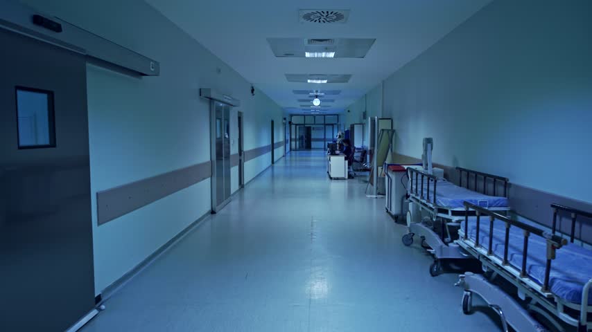 A long, dimly lit hospital corridor featuring rows of empty patient beds and sterile medical walls