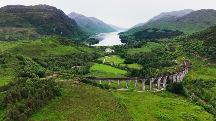 Aerial view of Glenfinnan Viaduct on the West Highland Line, with Loch Shiel and a green Scottish Highlands valley under cloudy skies in Scotland, United Kingdom. 4K UHD video.