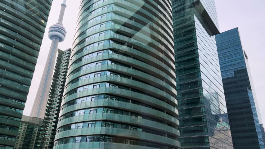 Low angle view of modern glass skyscrapers in Toronto financial district. High rise residential buildings and commercial office towers stand under clear sky. Contemporary urban architecture features curved glass facades and green tinted windows. Dense cityscape showcases progressive engineering and real estate development in Canada.