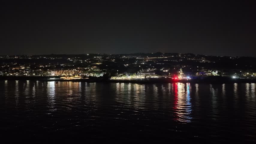 Nighttime coastal view of a sparkling sea reflecting colorful disco lights from a nearby vacation destination, showcasing the vibrant atmosphere along the shore. Concept of relaxation and resort life