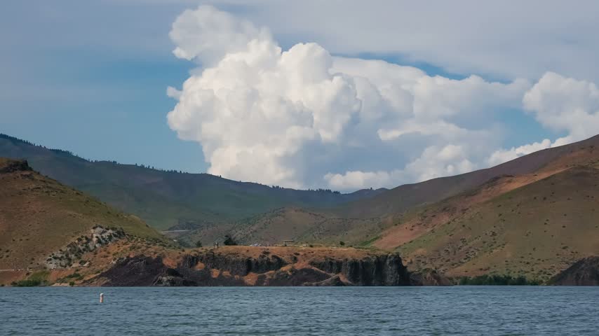View of Lucky Peak Lake surrounded by rolling hills and rocky terrain under a large cumulus cloud in Ada County, Idaho, United States.