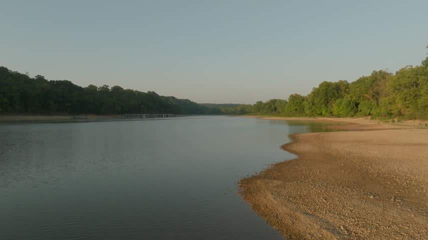 low altitude aerial view along lake shoreline showcasing morning light on one side and shadow shoreline on the other side