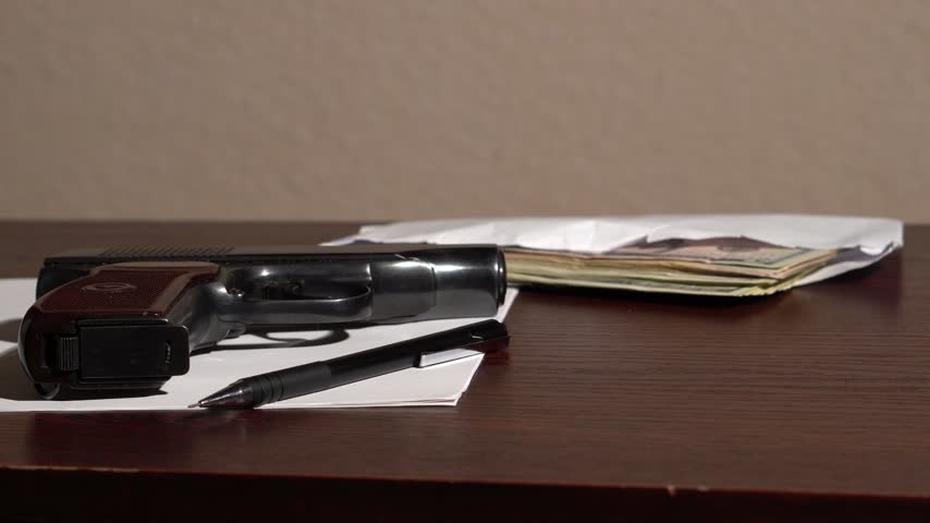 Unloading and handling a black pistol over a table where money and a white sheet of paper are lying.