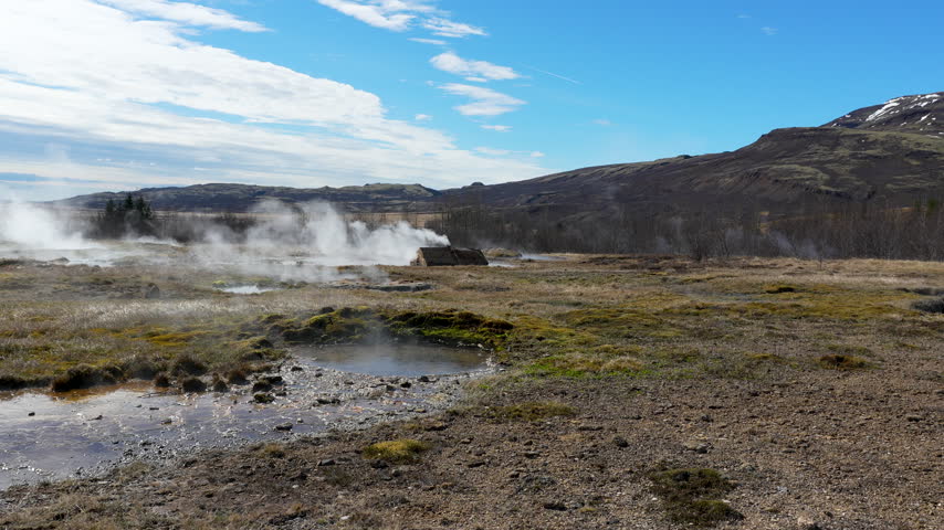 A wide shot of steaming geothermal vents and hot springs in the rugged Icelandic landscape near Geysir. Perfect for travel documentaries and sustainability content.