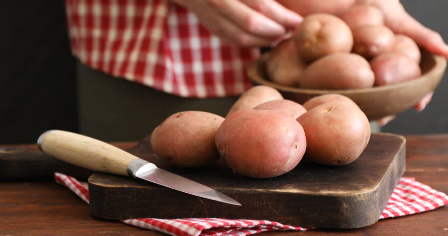 Woman putting ripe red potatoes onto board at table, closeup