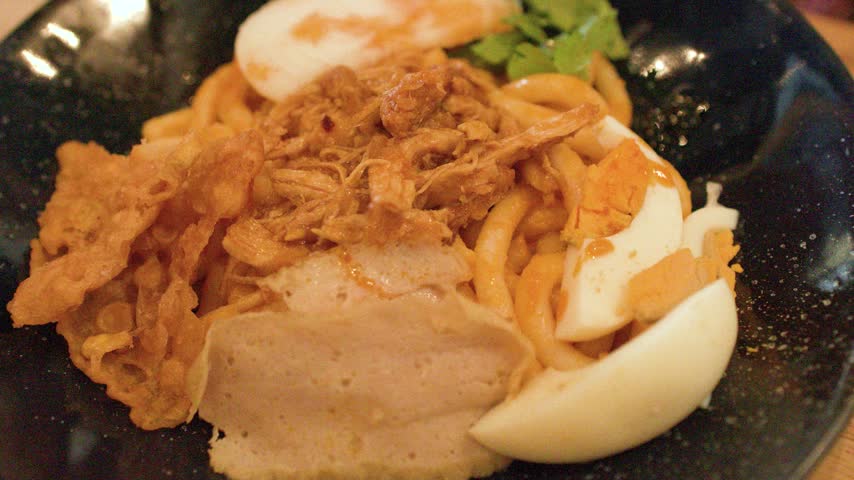 Close-up of chopsticks mixing traditional Burmese noodle salad with egg and chicken in Bangkok.