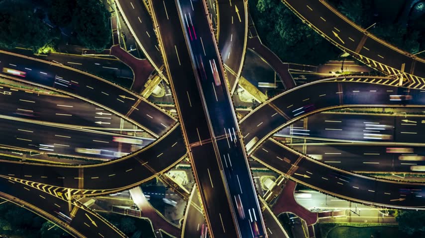 Stunning aerial long exposure captures a complex metropolitan highway interchange at night, featuring fast moving vehicles creating vibrant light streaks on busy roads.