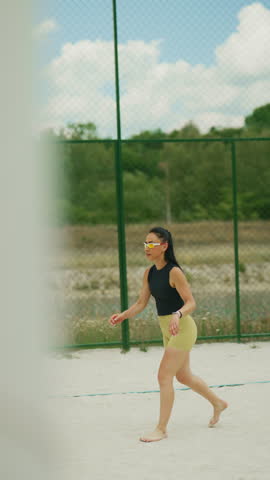 An athletic woman is actively playing beach volleyball on a sandy court. She trains outdoors, serving the ball with focus and enthusiasm during her fitness routine.