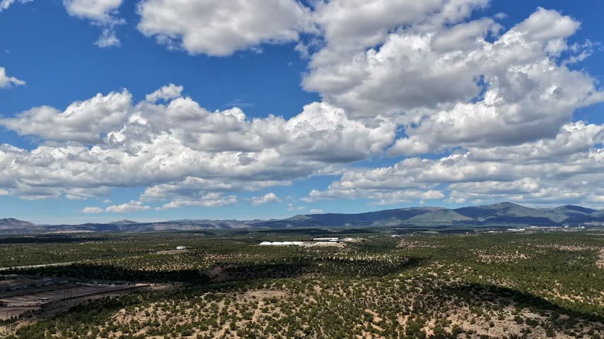 A 4k drone timelapse of the mesas of White Rock New Mexico with the Los Alamos National Laboratory hazard tents visible in the background under a cloudy blue sky.