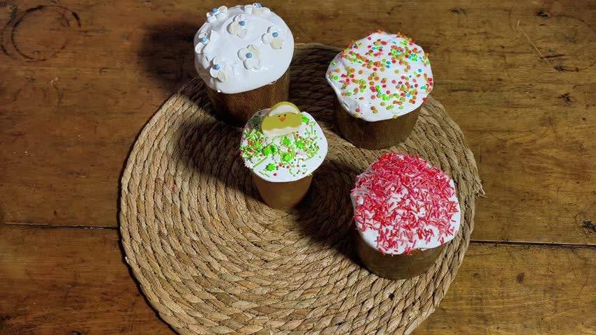 Top view of woman hands placing delicious easter cake on wooden table. Group of traditional easter cake with white icing and colorful sprinkles. Festive bakery for religious holiday celebration.
