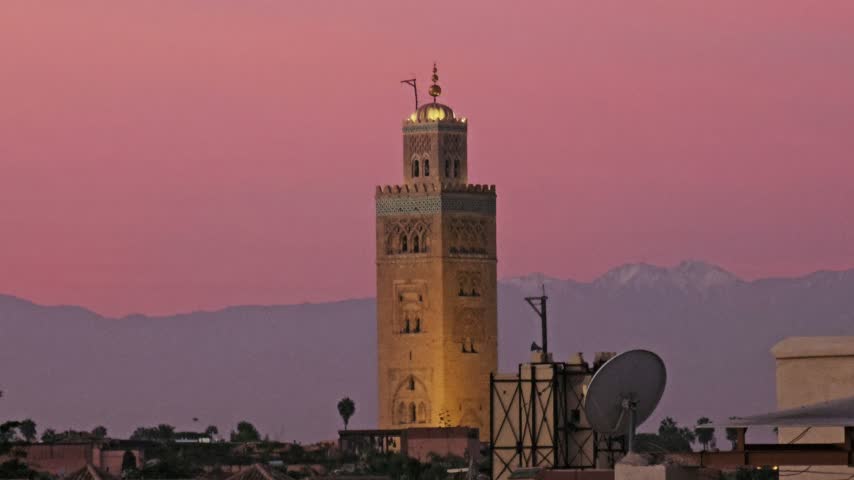 Illuminated Koutoubia Mosque minaret against a pink dusk sky with the snow-capped Atlas beyond, Marrakech, Morocco
