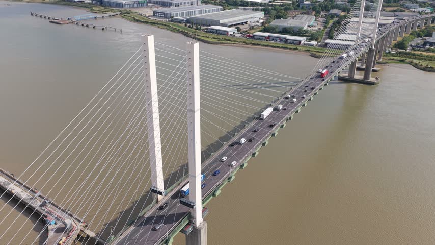 Cars and trucks travel across the Queen Elizabeth II Bridge over the River Thames during the day as commuters drive along the highway crossing the water towards the city center