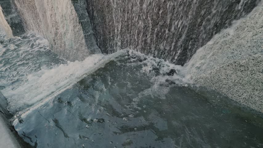 Static view of cascading fountain water beside a walkway and stairs.