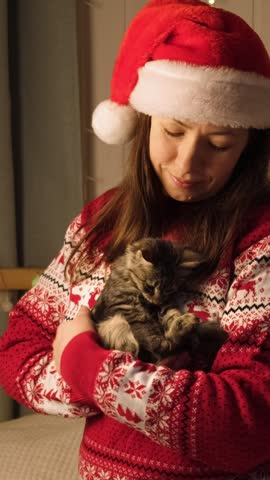 Young woman holdind and stroking a Cat. Kitten is a Christmas gift. Woman is happy and surprised. Cute pet is the best present. Holiday gifts concept. Festive decorations Background.
