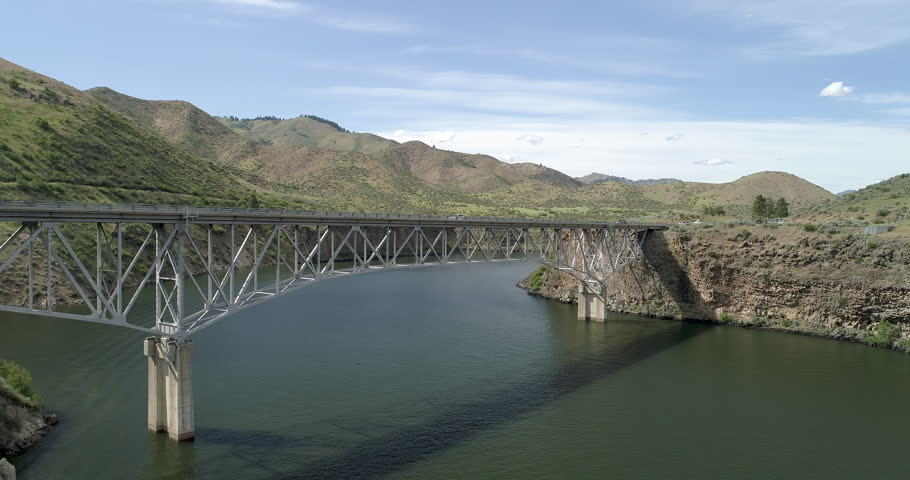 A bridge spans a river with a mountain in the background. The bridge is old and has a rustic appearance