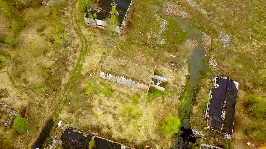 Aerial top-down view of abandoned concrete buildings overgrown with green vegetation and grass roofs in a desolate rural area